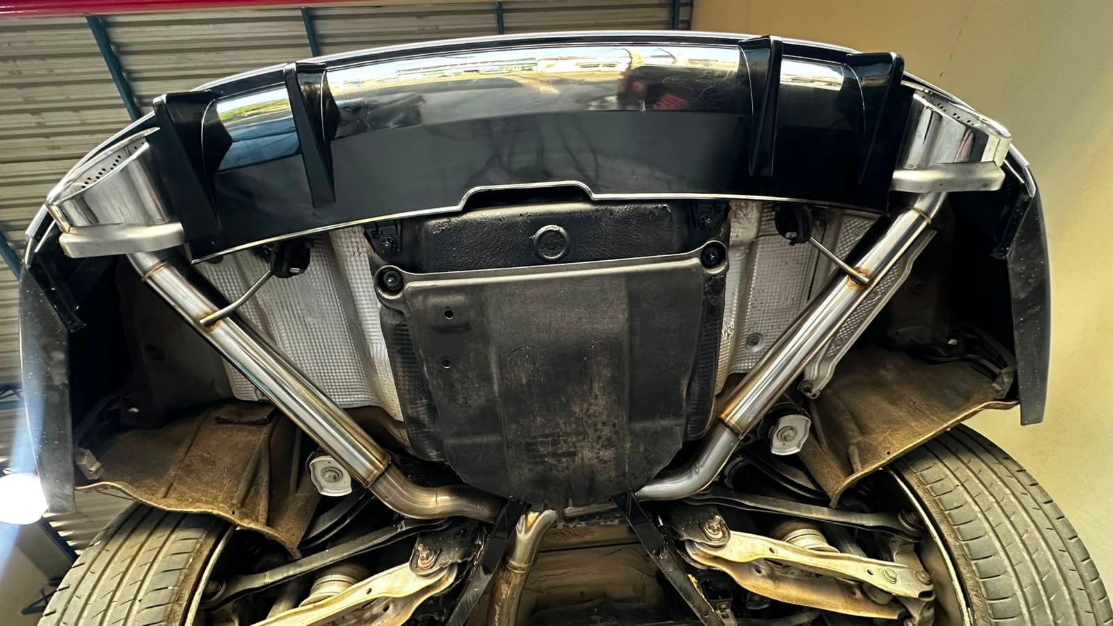 Sistema catback duplo em inox instalado sob a traseira de um carro esportivo preto com difusor