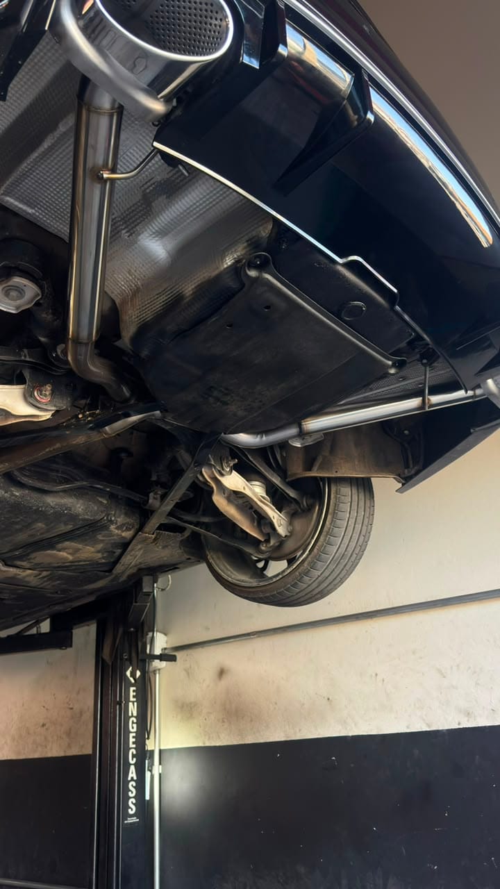 Tubo de escapamento em inox instalado sob a traseira de um carro preto na oficina